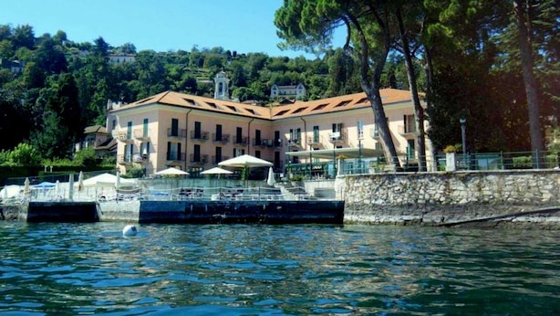 Ein Gebäude am Wasserufer mit mehreren Balkonen, einer Steinmauer und Booten, die im Wasser liegen.