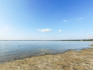 Un vaste lac aux eaux calmes, sous un ciel dégagé, avec une rive lointaine.