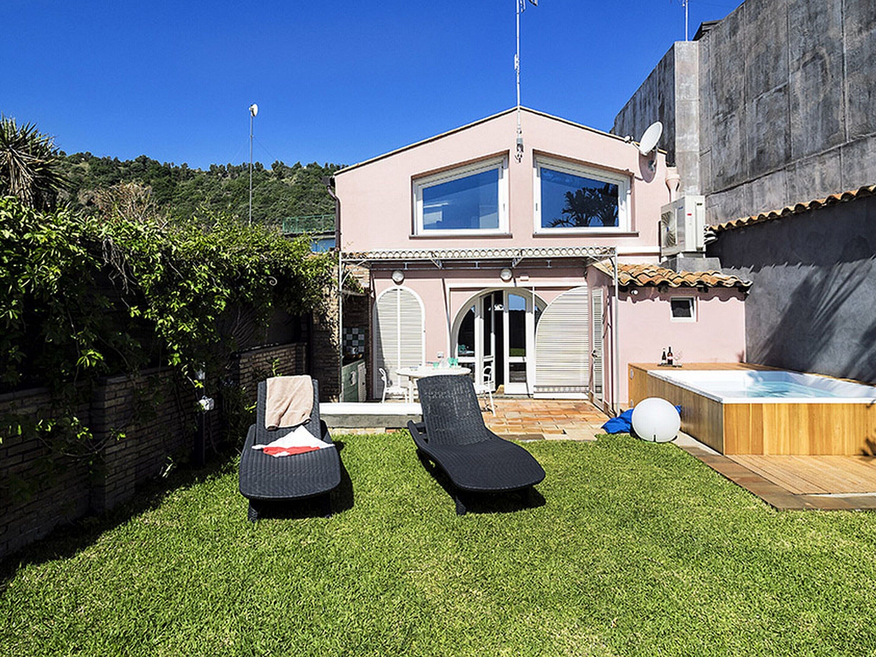 Une maison à deux étages dotée d’un patio comprenant deux chaises longues et un jacuzzi.