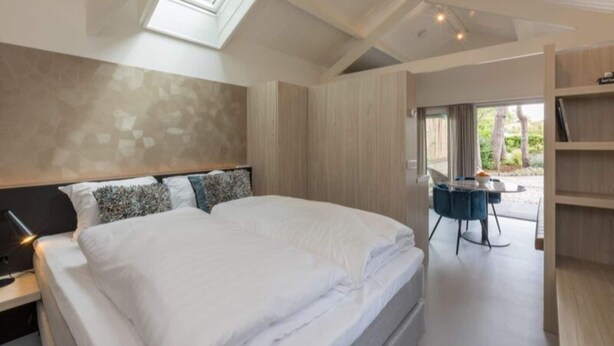 Une chambre avec un grand lit, une lucarne, un bureau avec une chaise et une vue sur l’extérieur.