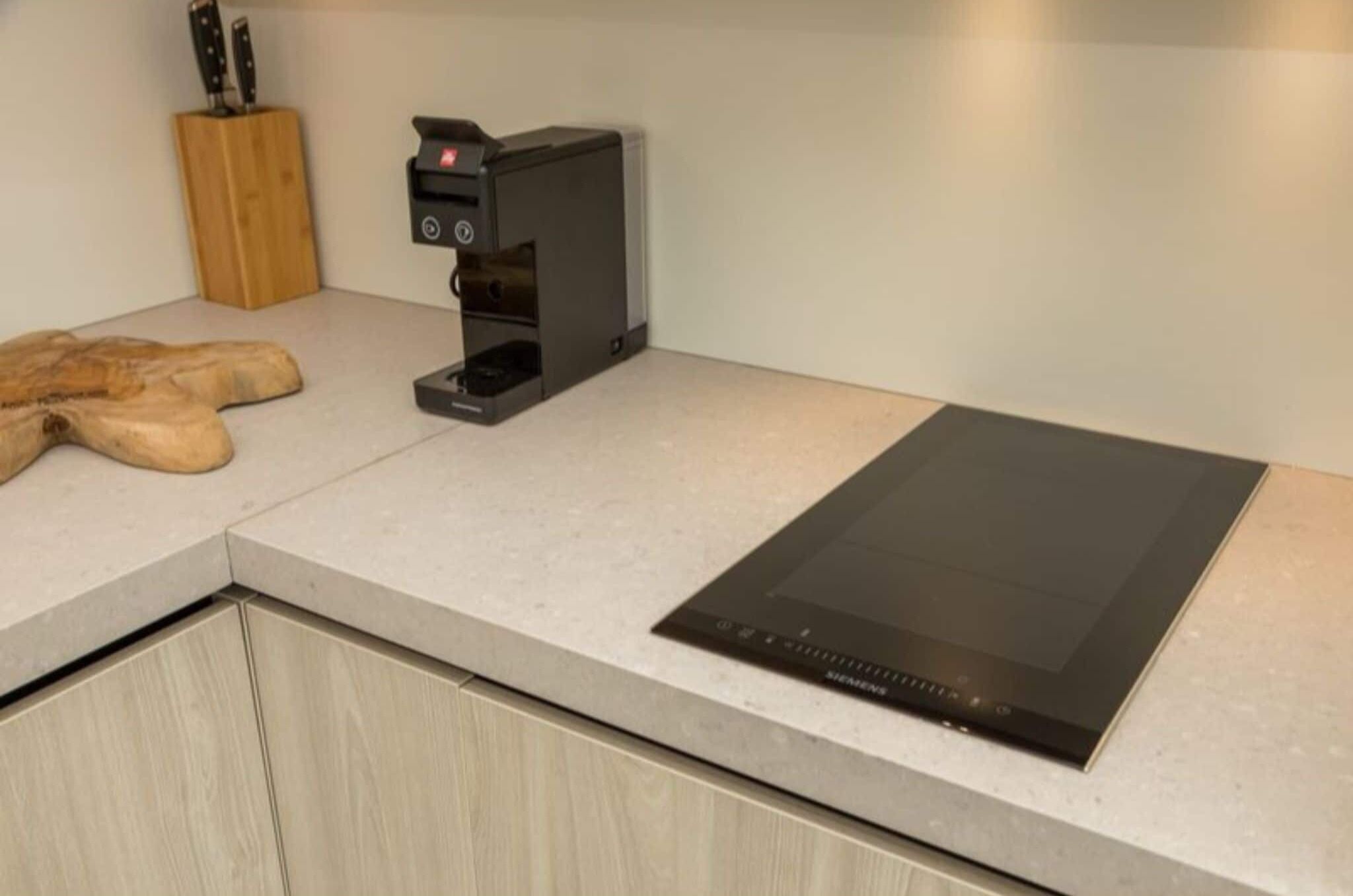 A kitchen with a built-in induction cooktop, a coffee machine, and a wooden cutting board.