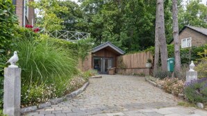 Un sentier pavé de pierres mène à un bâtiment en bois doté d’un toit en pente, entouré d’une végétation luxuriante et d’une clôture.