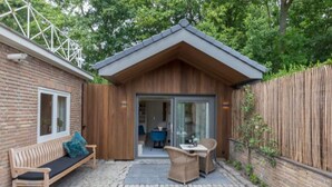 Une petite cabane en bois avec une façade en briques, une terrasse en bois, un banc et une table avec des chaises.