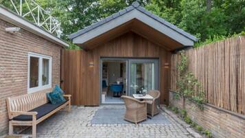 A small wooden cabin with a brick exterior, a wooden deck, a bench, and a table with chairs.