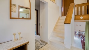 Eine Treppe führt zu einem Essbereich, ein Spiegel an der Wand und eine Holzbank mit einer Tischdecke aus Spitze.