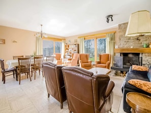 Een woonkamer met een open haard, een eethoek en uitzicht op de omgeving.