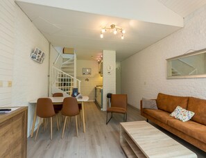 A compact living space with a dining area, a sofa, and a staircase leading to an upper level. - Nice Holiday Home in Quiet Park near Veerse Meer (Kortgene)
