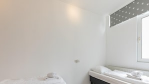 A room with two beds, one on each side of a central wall, with a window on the right and a door on the left.