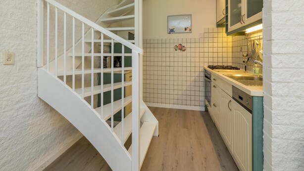 A kitchen with white cabinets, a wooden staircase, and a tiled backsplash.