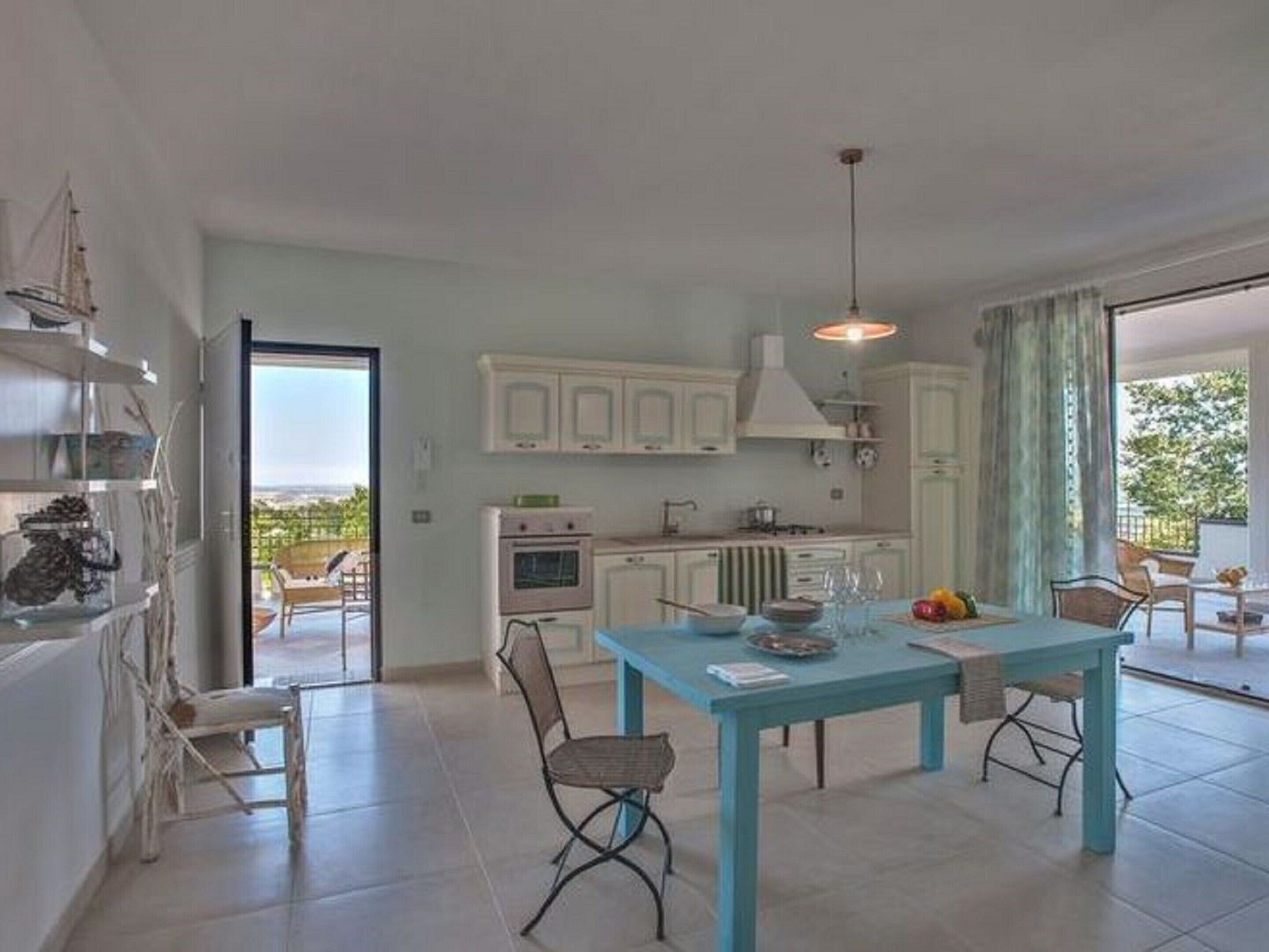 A modern kitchen with white cabinets, a dining table with chairs, and a view of the outdoors.