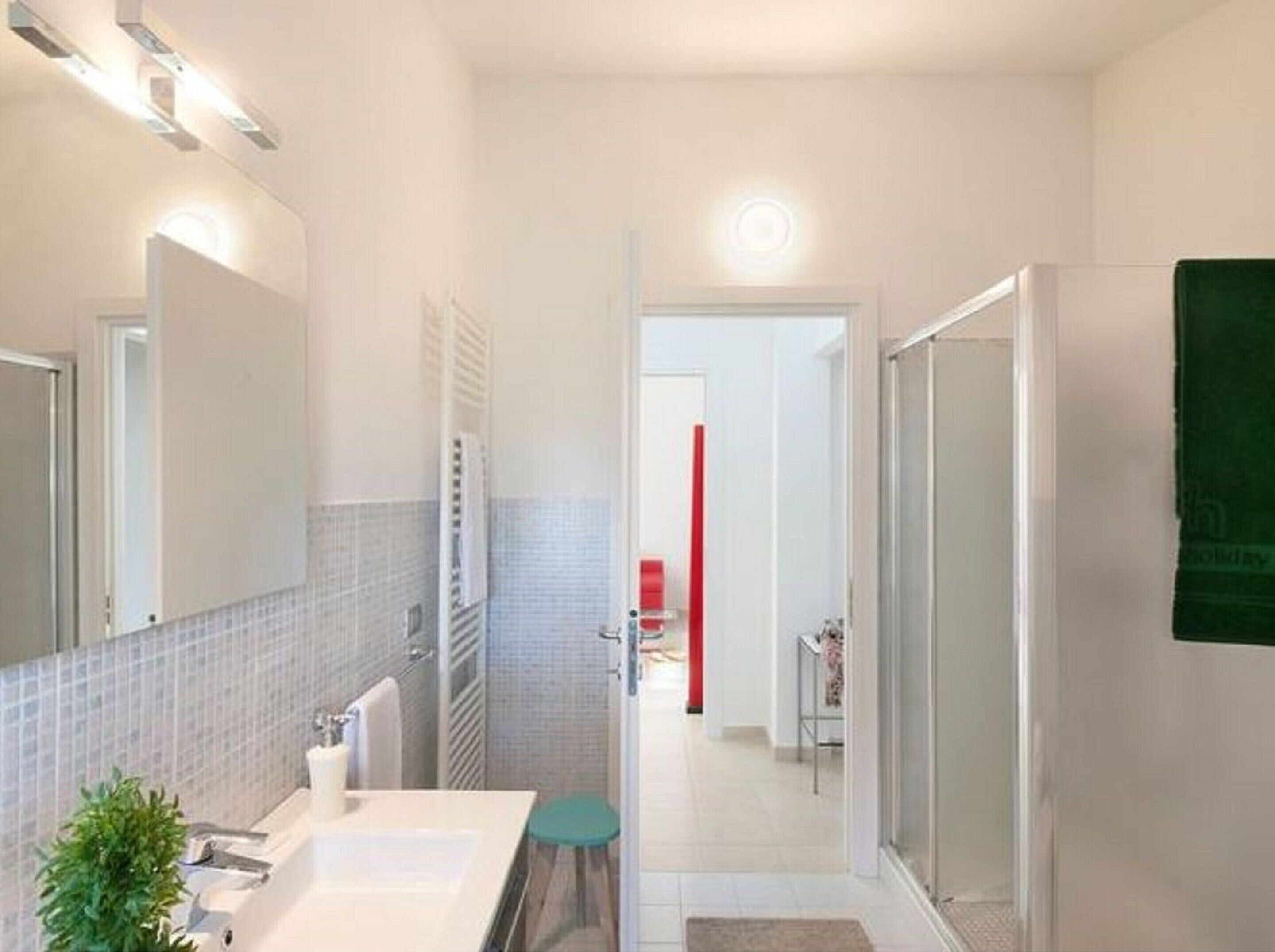 Une salle de bain moderne avec un lavabo blanc, un miroir, un porte-serviettes et un espace douche.