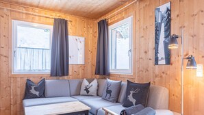 A cozy cabin interior with a wooden interior, a sofa with reindeer pillows, a table, and a lamp. - Chalet in Dachstein West With Shared Pool (Annaberg-Lungoetz)