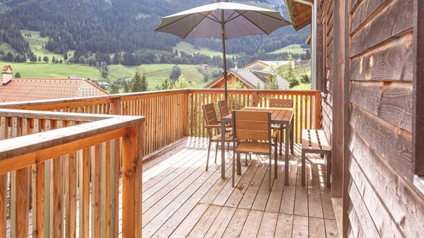 A wooden deck with a table and chairs, an umbrella, and a mountain view. - Chalet in Dachstein West With Shared Pool (Annaberg-Lungoetz)