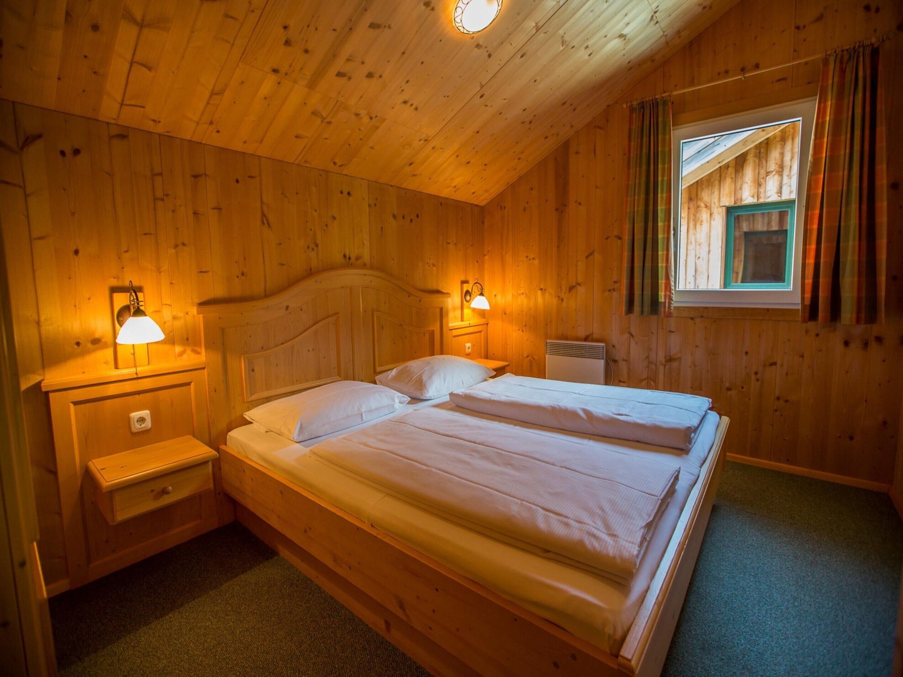 Ein Schlafzimmer einer Holzhütte mit zwei Betten, Nachttischen und einem Fenster mit Vorhängen.