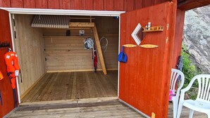 En træhytte med rødt ydre, trægulv, en stige og en hvid plastikstol udenfor.