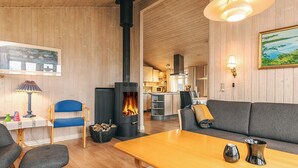 A cozy room with a wooden ceiling, a fireplace, a sofa, a table, and a kitchen in the background. - 6 Person Holiday Home in Lokken (Lokken)