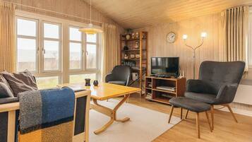 A cozy living room with a sofa, armchair, wooden coffee table, and a television on a stand.