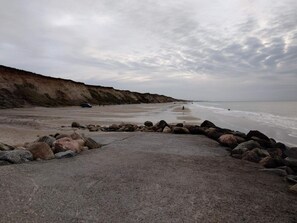 A beach with a rocky foreground, a cliff, and the ocean in the background. - 6 Person Holiday Home in Lokken (Lokken)