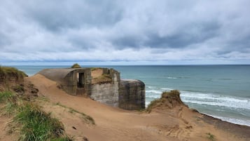 A coastal landscape with a sandy beach, a stone structure, and the ocean under a cloudy sky.