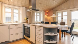 A modern kitchen with a central island, wooden cabinets, and a built-in oven. There are large windows providing natural light and a view of the outdoors. - 6 Person Holiday Home in Lokken (Lokken)