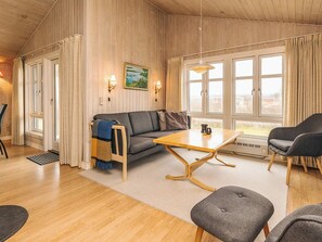 A cozy room with a sofa, a coffee table, and two chairs. There are windows with curtains, a painting on the wall, and a lamp. - 6 Person Holiday Home in Lokken (Lokken)