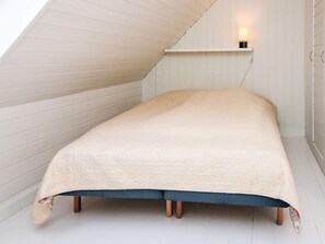 Ett litet, ombonat rum med ett sluttande tak, en enkel säng med ett randigt överkast och en väggmonterad lampa.