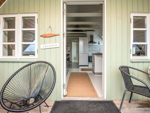 A green house with a welcome sign, two black chairs, and a kitchen visible through the open door. - 4 Person Holiday Home in Borkop (Borkop)