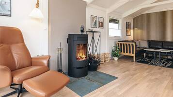 A modern living room with a leather chair, a black wood-burning stove, a sofa, and a dining table.