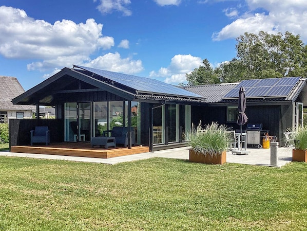 A modern house with solar panels, large glass windows, and a patio area.