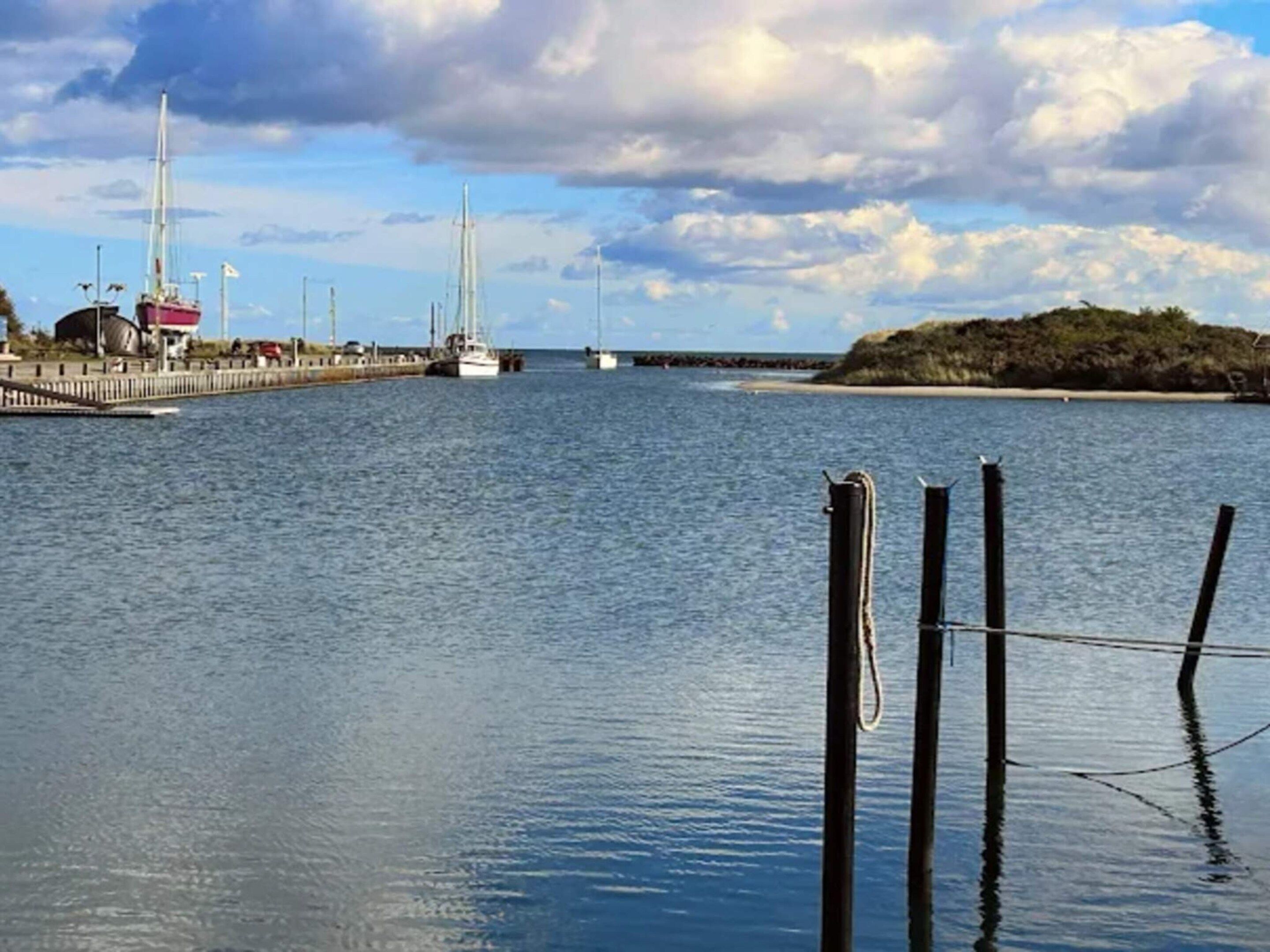 Ruhige Uferlandschaft mit einer Mole, Booten und einer kleinen Insel.