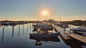 A marina with boats docked, calm water, and the sun setting in the background.
