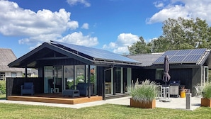 A modern house with large glass windows, a covered patio, and solar panels on the roof.
