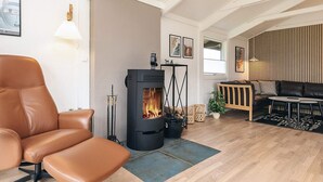 A modern living room with a leather chair, a black wood-burning stove, a sofa, and a dining table.