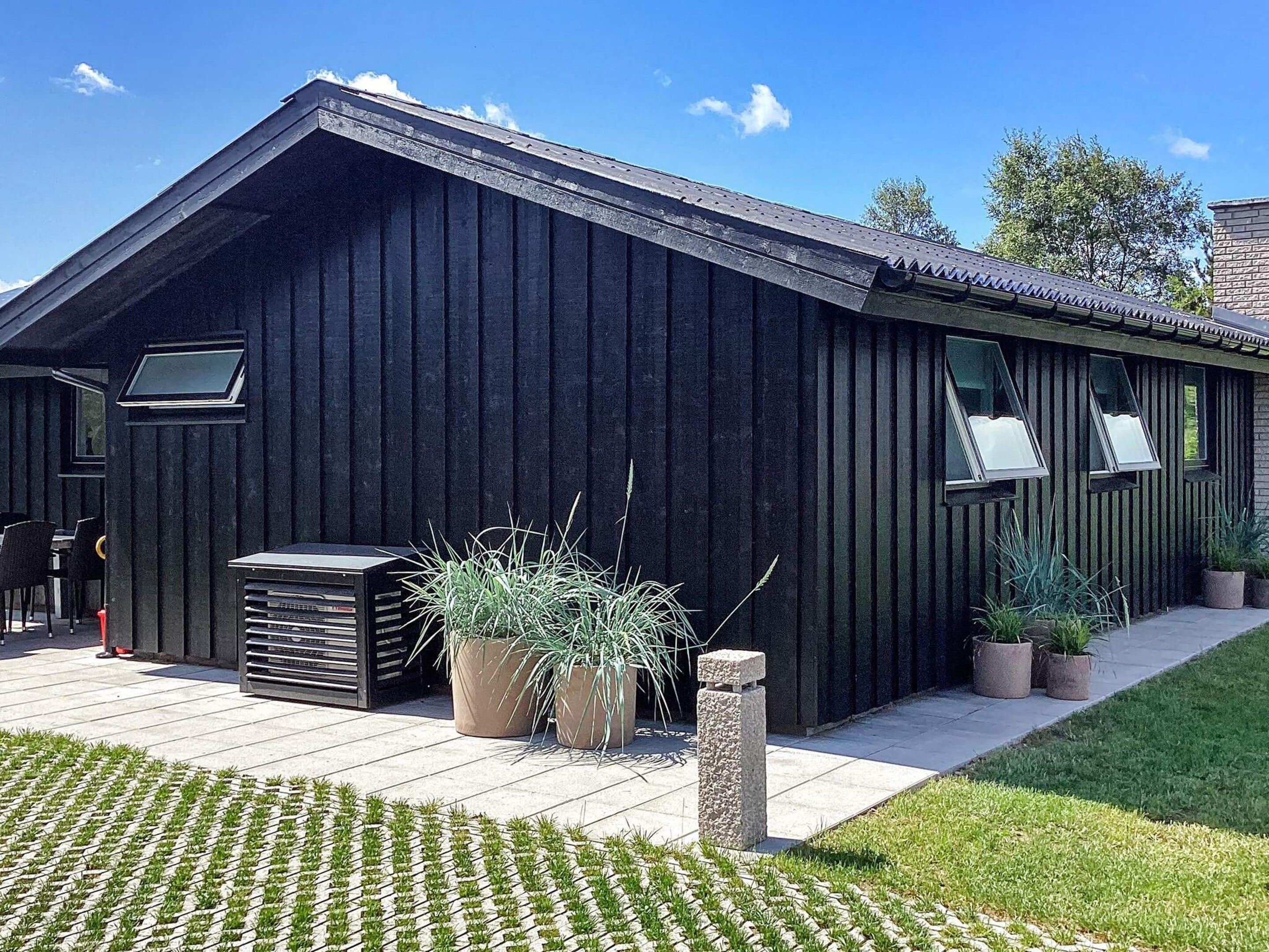 A modern building with a sloped roof, large windows, and a paved patio area with potted plants.