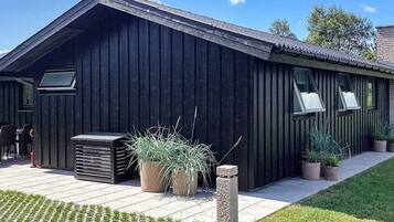A modern building with a sloped roof, large windows, and a paved patio area with potted plants.