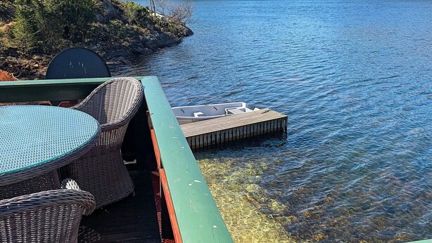 Terraza junto al lago con mobiliario de mimbre y un muelle flotante.