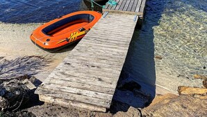 Un muelle de madera que se adentra en aguas claras, con un pequeño bote y una balsa inflable atados a él.