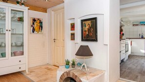 Eine Küche mit weißen Schränken, Fliesenboden, Kamin aus Backsteinen und einem Bild an der Wand.
