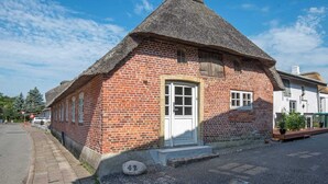 Ein traditionelles Backsteinhaus mit Strohdach, einer weißen Tür und einer kleinen Veranda.