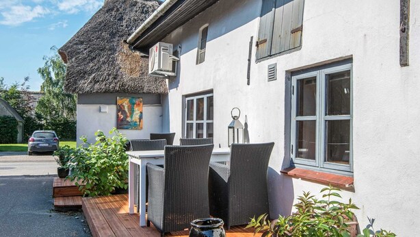 Ein Gebäude mit einem Strohdach, einer Terrasse mit Korbmöbeln und einer großen, schwarzen Vase.