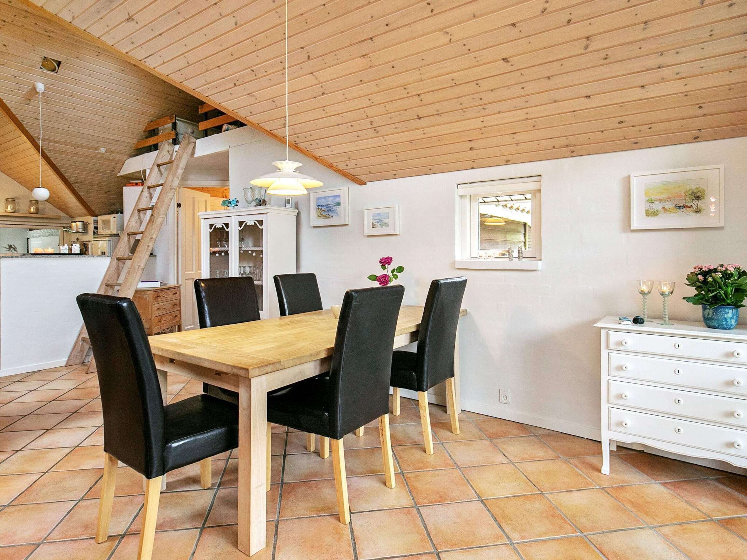 A dining area with a wooden table and chairs, a white cabinet, and a staircase leading to an upper level.
