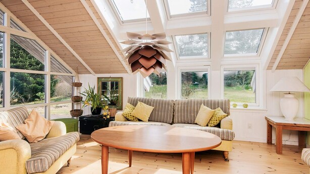A spacious room with a high ceiling, large windows, a round wooden table, and a sofa with striped cushions. - 7 Person Holiday Home in Ebeltoft (Ebeltoft)