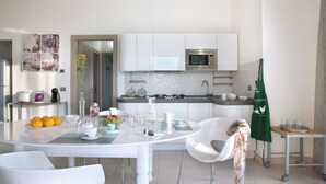A modern kitchen with white cabinets, a microwave, and a dining area with a white table and chairs. - Grand Villa in Tavullia (Tavullia)