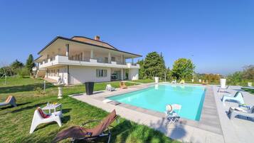 A large house with a swimming pool, outdoor seating, and a well-maintained lawn.