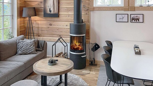 L’intérieur chaleureux d’un chalet avec un poêle à bois, un canapé, une table ronde et un coin repas.
