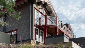 Une maison d’angle avec des fondations en pierre, un balcon doté d’une rambarde rouge et de grandes fenêtres.