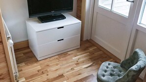 Une pièce avec une commode blanche, un téléviseur à écran plat posé dessus, et deux fauteuils à accoudoirs capitonnés.