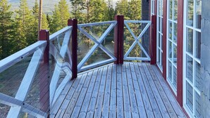 Une terrasse en bois avec une rambarde en verre donnant sur une zone boisée.