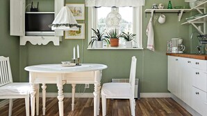 A kitchen with a round table, white chairs, a window with plants, and a white cabinet. - 2 Person Holiday Home in Rimforsa (Rimforsa)