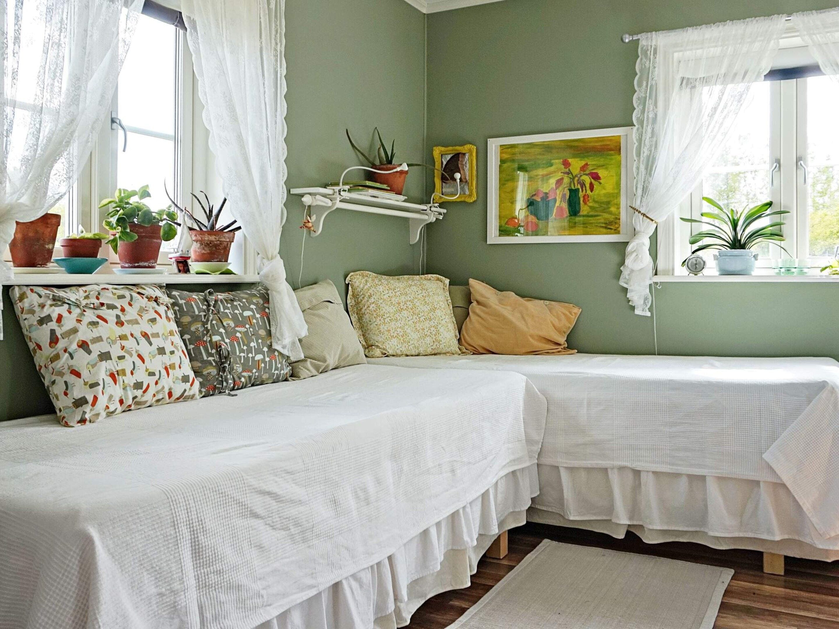 A room with two beds, a bedside table with plants, a painting, and a window with curtains.